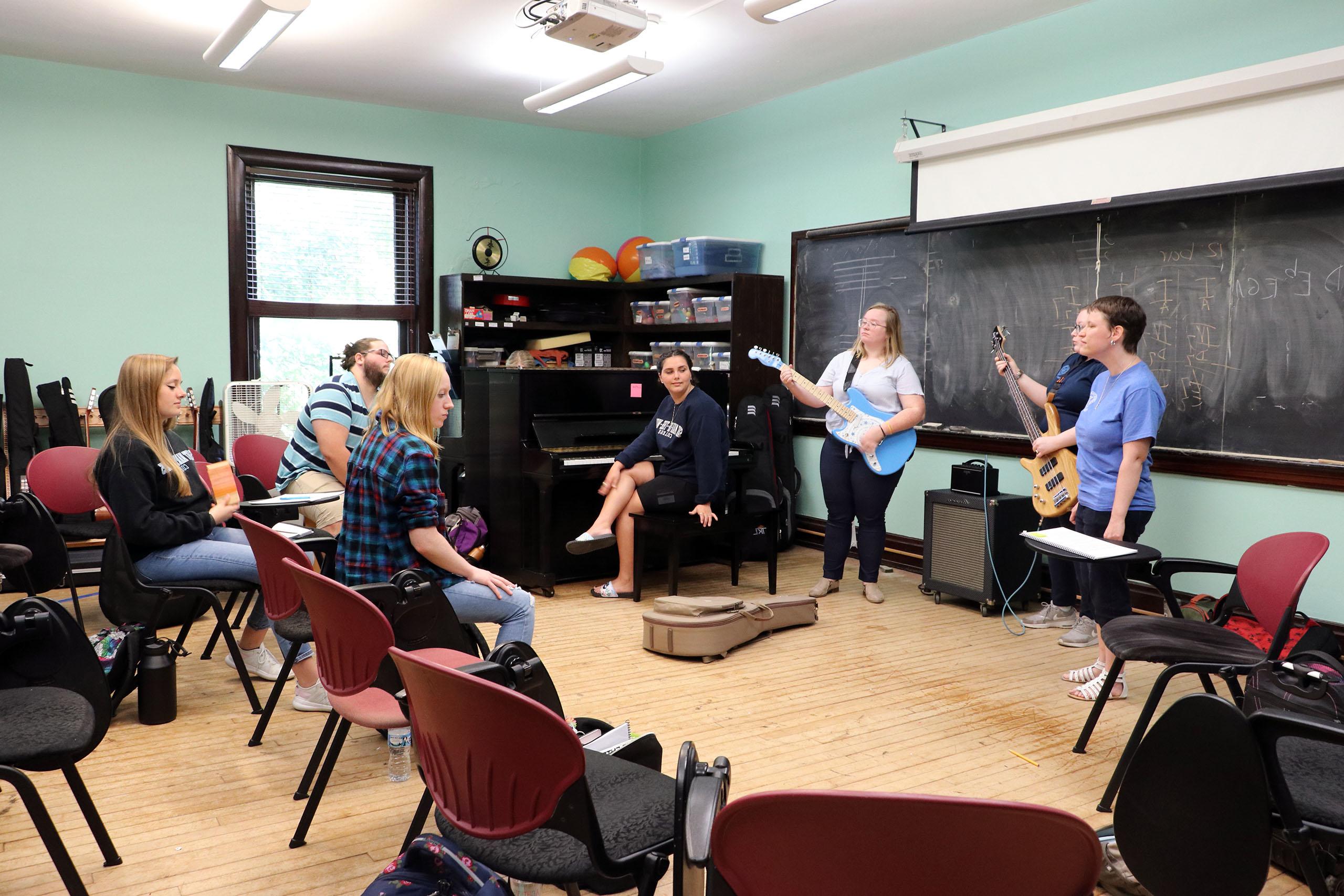 A music class with two people playing guitars, a student singing, and four students listening